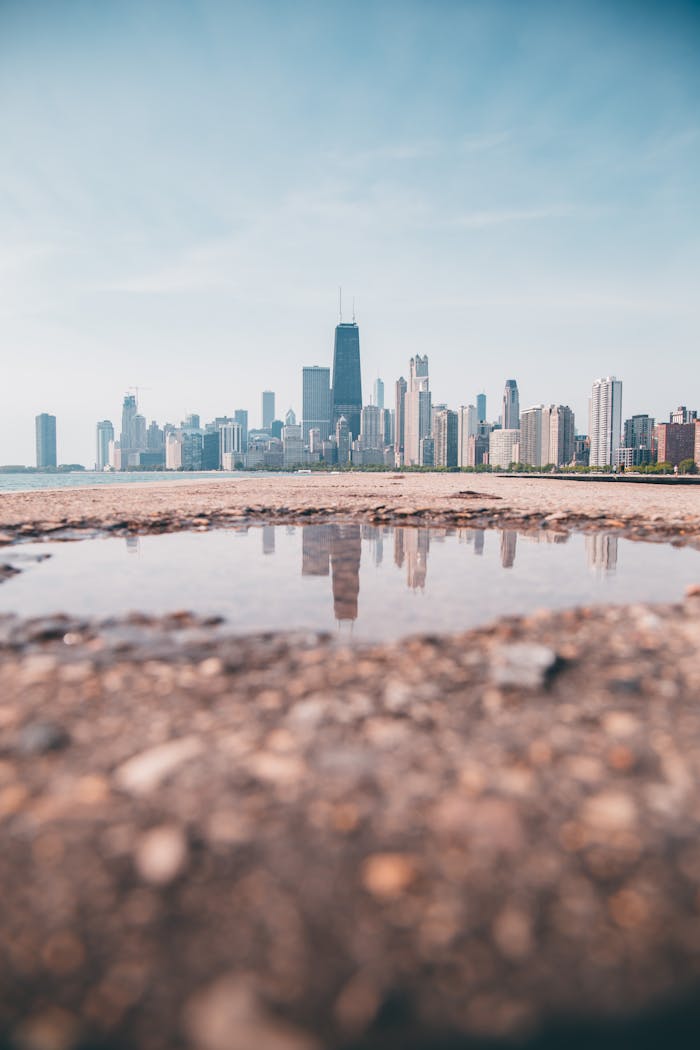 Iconic Chicago skyline reflected in puddle on a sunny day.
